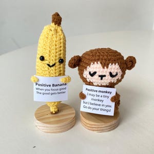 Könnte beinhalten: Zwei gehäkelte Plüschtiere, eine Banane und ein Affe, halten Schilder mit positiven Botschaften. Die Banane sagt "Positive Banana When you focus good The good gets better". Der Affe sagt "Positive monkey I may be a tiny monkey but I believe in you. Go do your things!"
