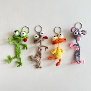 May include: Four quirky crochet animal keyrings. A green frog with a red tongue, a tan lizard, a yellow duck with an orange beak and feet, and a grey mouse with pink ears and paws. Each keyring has a silver ring.