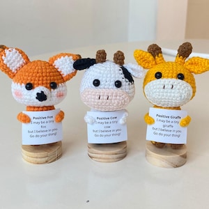 May include: Three crocheted animal figurines holding signs with positive messages. A fox, cow, and giraffe are each holding a sign with a message about believing in yourself and doing your thing.