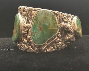 May include: A silver ring with three green turquoise stones set in a textured band.