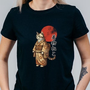 以下が含まれることがあります： 着物ねこが描かれた黒いTシャツ。猫は伝統的な日本の着物を着ており、後ろには赤い太陽が描かれている。