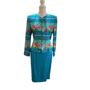 May include: A two-piece teal suit with a floral print jacket and a matching skirt. The jacket features a button-up front and long sleeves. The floral pattern includes pink, yellow, and purple flowers. The skirt is a solid teal color.