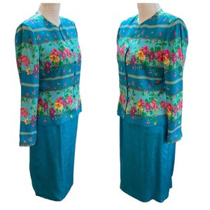 May include: A two-piece teal suit featuring a floral print jacket and a matching skirt. The jacket has a V-neck, long sleeves, and a button-down front. The floral pattern includes pink, yellow, and purple flowers. The skirt is a solid teal color.
