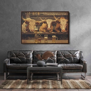 May include: A framed artwork depicts three longhorn cattle at a bar, each with a glass of beer. The bar features bottles and glasses, with a shelf of liquor bottles in the background. The artwork is displayed above a black leather couch.