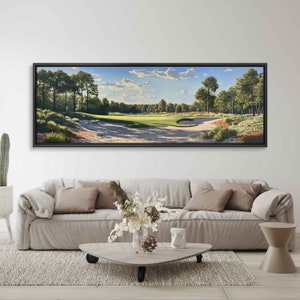May include: A framed landscape painting of a golf course, featuring a green fairway, sand traps, and trees under a blue sky with clouds. The artwork is displayed above a beige sofa in a living room setting.