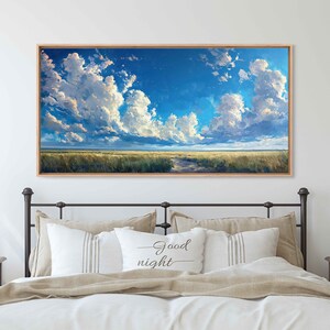 May include: A framed landscape painting of a field with a path leading to a horizon under a blue sky with white clouds. The painting is hanging above a bed with a pillow that says "Good night".