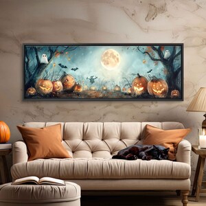 May include: A long, horizontal painting depicting a Halloween scene with a full moon, a ghost, and a row of lit jack-o'-lanterns. The painting is framed in black and hangs on a wall above a beige couch.