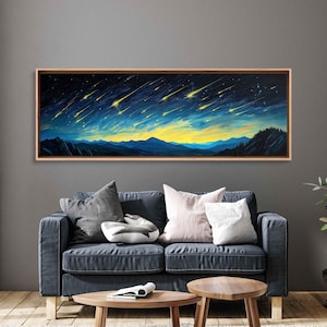 May include: A framed landscape painting depicts a night sky filled with yellow shooting stars over blue mountains and a yellow and blue horizon. The artwork is displayed above a dark blue sofa with pillows and wooden tables.