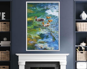 May include: A framed art print depicts a family of ducks swimming in a vibrant, impressionistic river scene. The artwork features a mother duck and three ducklings, with a palette of blues, greens, and yellows. The frame is white.