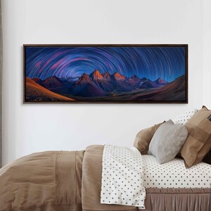 May include: A framed panoramic canvas print featuring a mountain range under a night sky. The image showcases star trails in shades of blue, purple, and pink, arching over the peaks. The mountains are illuminated with warm orange and yellow hues.