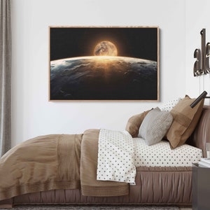 May include: A framed photograph of a large, bright moon rising over a planet's horizon. The moon is partially obscured by clouds, and the planet's surface is visible in the distance. The photograph is displayed on a wall above a bed with brown and white bedding.