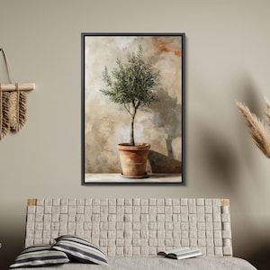 May include: A framed painting of a small olive tree in a terracotta pot against a textured beige wall. The tree has green leaves and a long, slender trunk. The painting is in a black frame.