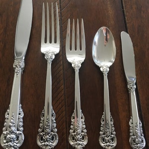 Può includere: Set di cinque posate in argento placcato, tra cui un coltello, due forchette e due cucchiai. I manici sono decorati con un motivo floreale.