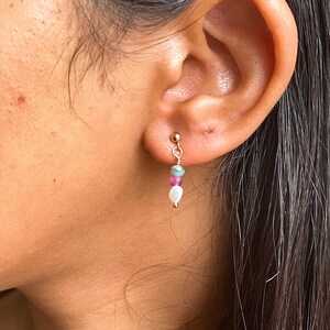 Könnte beinhalten: Goldene Ohrhänger mit einer weißen Perle, rosa und grünen Edelsteinperlen.