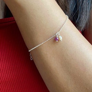 Peut inclure: Un bracelet délicat en chaîne argent avec une petite pierre précieuse violette et un charme en perle.