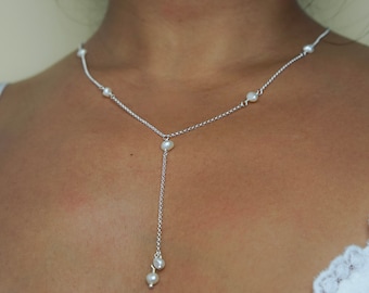 Può includere: Una delicata collana d'argento con un design a forma di Y. La collana presenta piccole perle rotonde distanziate lungo la catena e alla fine della goccia. La collana è mostrata sul collo di una persona, evidenziando la sua elegante semplicità.