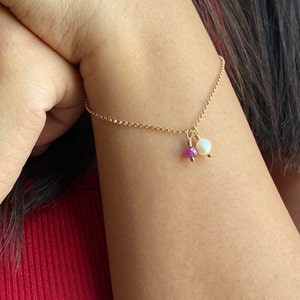Könnte beinhalten: Ein zartes Armband aus einer goldenen Kette mit einem kleinen rosafarbenen Edelstein und einem weißen Perlenanhänger.