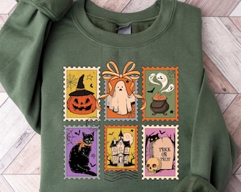 May include: Green sweatshirt featuring a Halloween-themed design. The design includes six postage stamp-style illustrations with a pumpkin, ghost, cauldron, black cat, haunted house, and a tombstone with the text "Trick or Treat".