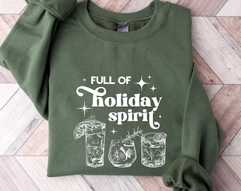 Puede incluir: Sudadera verde con un gráfico blanco que dice "Full of holiday spirit" con tres vasos de cóctel.
