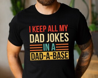 May include: A black t-shirt with a vintage-style graphic that reads "I keep all my dad jokes in a dad-a-base".