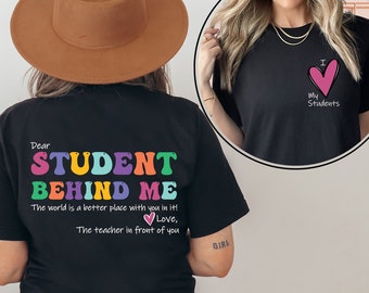 May include: Black t-shirt with the text "Dear Student Behind Me The world is a better place with you in it! Love, The teacher in front of you" in colourful letters. The back of the shirt has a pink heart with the text "I My Students".