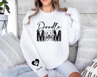 May include: White sweatshirt with the text "Doodle Mom" in black script and block letters, featuring a doodle dog illustration. A black heart with a paw print and the name "Charlie" is on the sleeve.