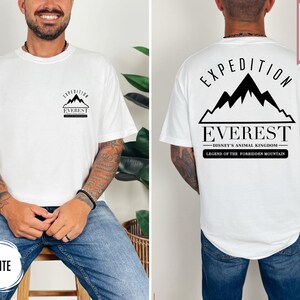 Op de afbeelding: Wit T-shirt met een zwarte afbeelding van een bergketen en het woord "EVEREST". De achterkant van het shirt heeft de tekst "EXPEDITION EVEREST DISNEY'S ANIMAL KINGDOM LEGEND OF THE FORBIDDEN MOUNTAIN". Het shirt is gelabeld "SUPER SOFT".