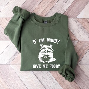 May include: Green sweatshirt with a white graphic of a raccoon and the text "If I'm Moody Give Me Foody".