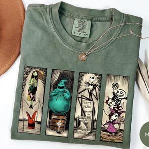 May include: Moss green Comfort Colors t-shirt featuring four framed illustrations of characters from a popular animated film. A gold necklace rests on the shirt. A brown hat and dried leaves are in the background.