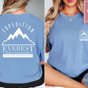 Op de afbeelding: Lichtblauw T-shirt met de tekst "EXPEDITION EVEREST" en een bergafbeelding. De achterkant van het shirt heeft hetzelfde ontwerp, met de tekst "DISNEY'S ANIMAL KINGDOM" en "LEGEND OF THE FORBIDDEN MOUNTAIN".