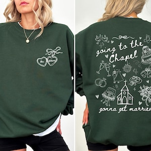 K&ouml;nnte beinhalten: Ein dunkelgr&uuml;nes Sweatshirt mit wei&szlig;em Text und Grafiken. Die Vorderseite zeigt ein herzf&ouml;rmiges Design mit dem Text "Mrs. Wilson". Auf der R&uuml;ckseite steht der Satz "going to the Chapel gonna get married" mit Illustrationen zum Thema Hochzeit.