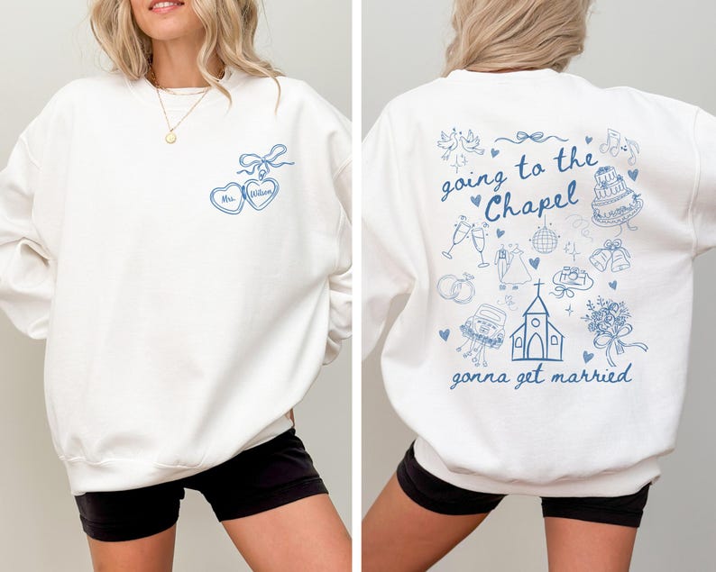 K&ouml;nnte beinhalten: Wei&szlig;es Sweatshirt mit blauem Grafiktext und Illustrationen. Die Vorderseite zeigt zwei herzf&ouml;rmige Anh&auml;nger mit dem Text "Mrs. Wilson". Auf der R&uuml;ckseite steht der Satz "going to the Chapel gonna get married" mit Hochzeitsmotiven.