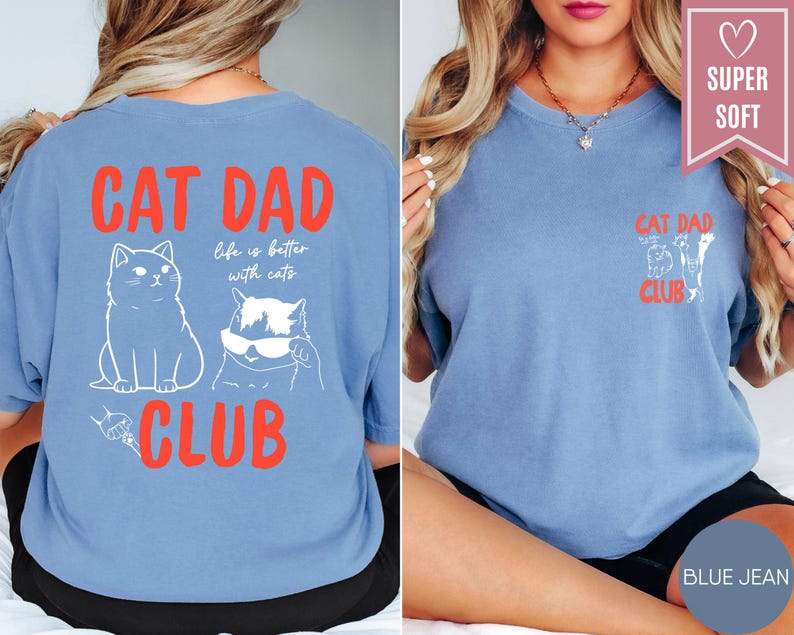 May include: Blue jean colored t-shirts with the text "CAT DAD CLUB" in red. The back of the shirt features a cat illustration and the phrase "life is better with cats." The front of the shirt has a smaller "CAT DAD CLUB" design.