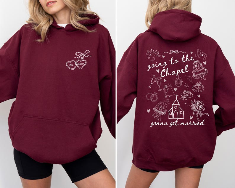 K&ouml;nnte beinhalten: Ein weinroter Kapuzenpullover mit wei&szlig;en grafischen Texten und Illustrationen. Die Vorderseite zeigt zwei herzf&ouml;rmige Designs mit dem Text "Mrs. [Name]" im Inneren. Auf der R&uuml;ckseite steht der Satz "going to the Chapel gonna get married" mit Illustrationen zum Thema Hochzeit.