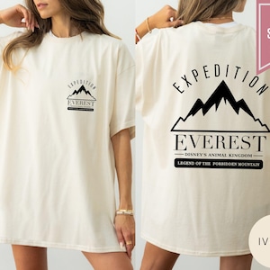 Op de afbeelding: Ivoor kleurig T-shirt met zwarte tekst en bergontwerp. De voorkant heeft een kleine bergafbeelding met de tekst "EXPEDITION EVEREST". De achterkant toont een grotere bergafbeelding met de tekst "EXPEDITION EVEREST" en "DISNEY'S ANIMAL KINGDOM".