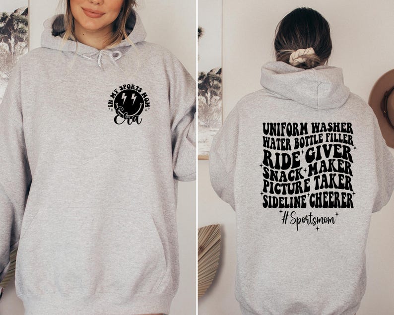 Pode incluir: Camisola de moletom cinza com capuz com texto preto que diz "In my sports mom era" na frente e "Uniform washer, water bottle filler, ride giver, snack maker, picture taker, sideline cheerleader #sportsmom" nas costas.