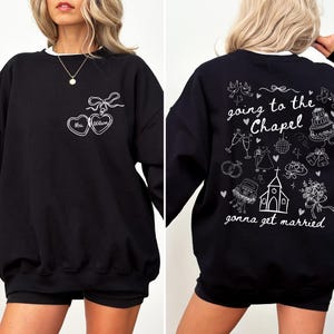K&ouml;nnte beinhalten: Schwarzes Sweatshirt mit wei&szlig;em Besatz. Auf der Vorderseite befindet sich ein Herzdesign mit "Mrs. William" und einer Schleife. Auf der R&uuml;ckseite steht der Satz "going to the chapel gonna get married" mit Hochzeitsillustrationen.