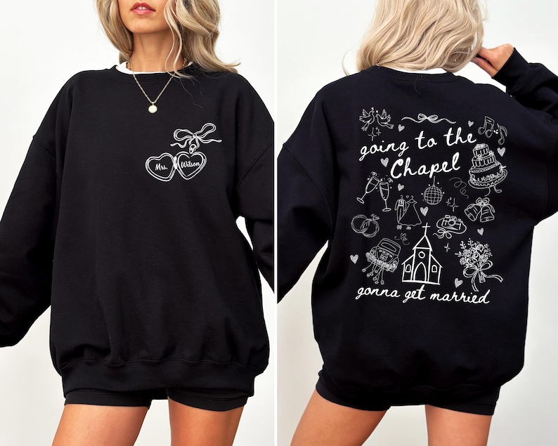 K&ouml;nnte beinhalten: Schwarzes Sweatshirt mit wei&szlig;em Besatz. Auf der Vorderseite befindet sich ein Herzdesign mit "Mrs. William" und einer Schleife. Auf der R&uuml;ckseite steht der Satz "going to the chapel gonna get married" mit Hochzeitsillustrationen.