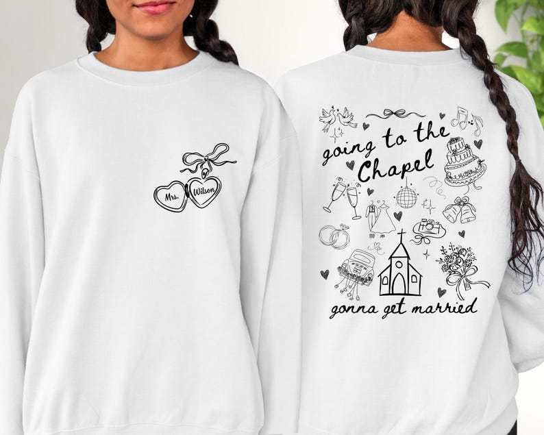 K&ouml;nnte beinhalten: Wei&szlig;es Sweatshirt mit schwarzer Strichzeichnung. Auf der Vorderseite befindet sich ein herzf&ouml;rmiges Medaillon mit der Aufschrift "Mrs. Wilson". Auf der R&uuml;ckseite steht der Satz "going to the Chapel, gonna get married" mit Illustrationen zum Thema Hochzeit.