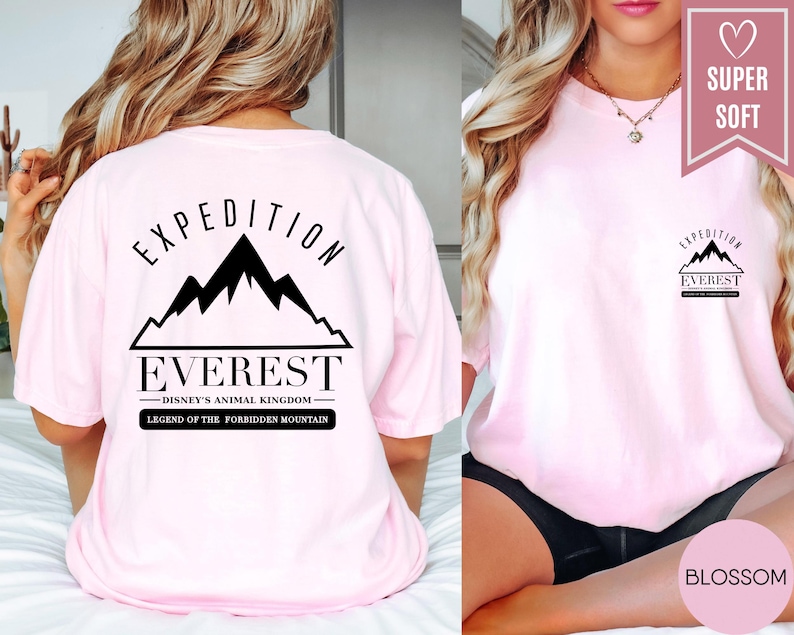 Op de afbeelding: Een lichtroze t-shirt met de tekst "EXPEDITION EVEREST" en een bergafbeelding. Het shirt heeft ook de tekst "DISNEY'S ANIMAL KINGDOM LEGEND OF THE FORBIDDEN MOUNTAIN". Het shirt is gelabeld met "SUPER SOFT" en "BLOSSOM".