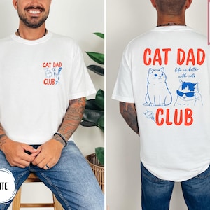 May include: White t-shirt with "CAT DAD CLUB" printed in red and blue. The front features a small graphic of cats, while the back displays two cats and the phrase "Life is better with cats." The shirt is labeled "SUPER SOFT."