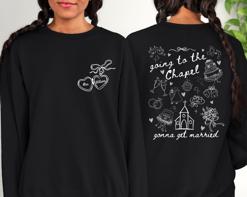 K&ouml;nnte beinhalten: Schwarzes Sweatshirt mit wei&szlig;er Strichzeichnung. Auf der Vorderseite befinden sich zwei verbundene herzf&ouml;rmige Designs mit dem Text "Mrs. Wilson". Auf der R&uuml;ckseite steht der Satz "going to the Chapel, gonna get married" mit Illustrationen zum Thema Hochzeit.