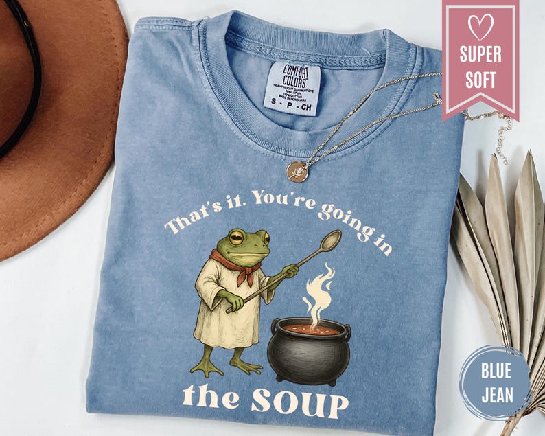May include: Blue jean Comfort Colors t-shirt with a frog chef graphic holding a spoon over a pot of soup. The text reads "That's it. You're going in the soup."