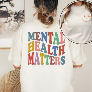 May include: A white t-shirt with the text "MENTAL HEALTH MATTERS" in rainbow colors on the back. The front of the shirt has the text "Be Kind To Your Mind" with a smiley face.