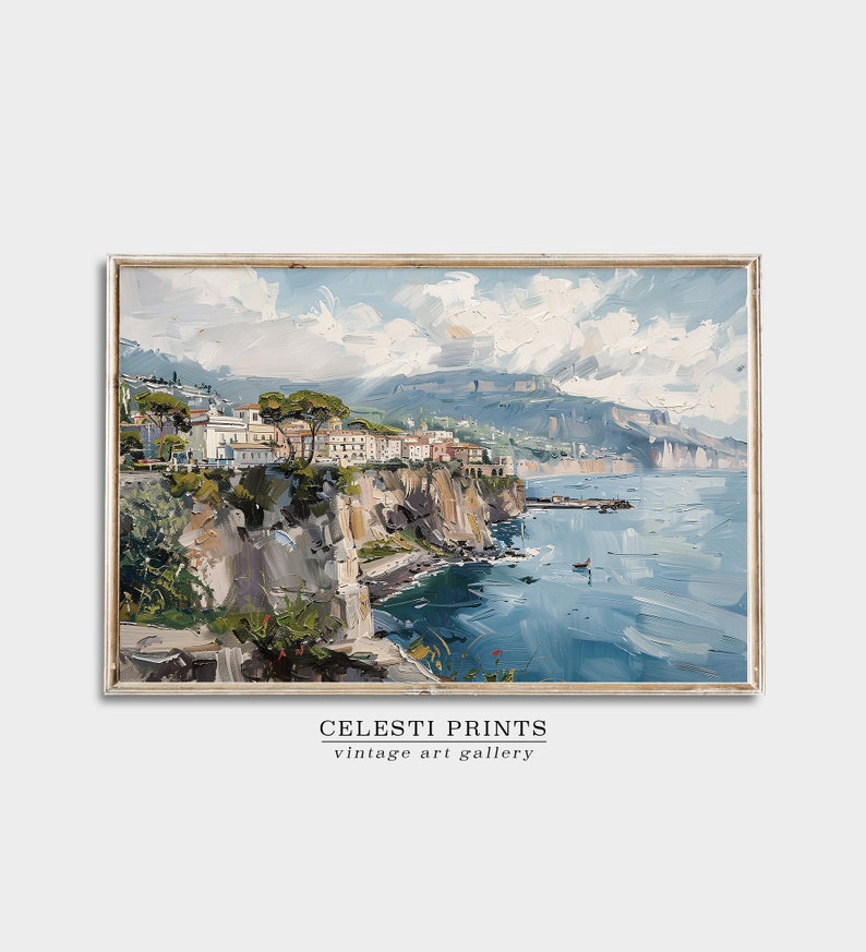 May include: A painting of a coastal town with white buildings on a cliff overlooking a blue sea. The sky is a light blue with white clouds. The painting is framed in a light wood frame.