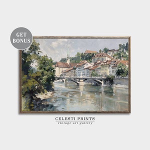 May include: A painting of a city scene with a river and bridge. The buildings are painted in a light brown color with white trim. The river is a light blue color and the bridge is a dark brown color. The painting is framed in a gold frame.