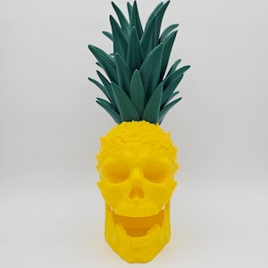May include: A yellow skull planter with a green pineapple top. The skull has a wide open mouth and is made of plastic.