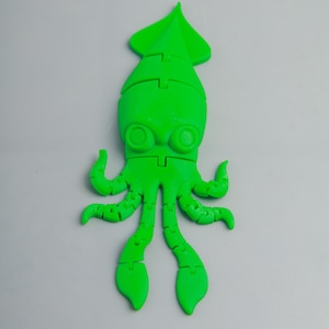 Könnte beinhalten: Ein grünes, 3D-gedrucktes Tintenfischspielzeug mit segmentierten Armen und einem großen Kopf mit zwei Augen.