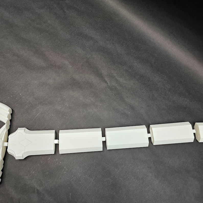 May include: A white, segmented object with a geometric design. The object is composed of rectangular and diamond-shaped components, connected in a linear fashion. The item is set against a dark background.