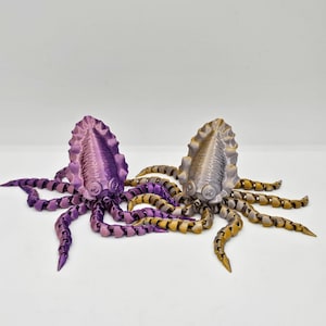 Könnte beinhalten: Zwei 3D-gedruckte Oktopus-Figuren mit segmentierten Beinen. Ein Oktopus ist lila und der andere ist golden.